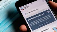 Eine Hand hält ein Smartphone, auf dem die Corona-Warn-App der Bundesregierung angezeigt wird