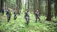Mehrere Soldaten und Soldatinnen laufen einen Abhang im Wald hinunter.