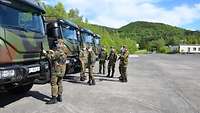 Soldaten des Landesregiments Bayern im Feldanzug stehen in der Sonne vor grünen Lastwagen, im Hintergrund ein Berg.