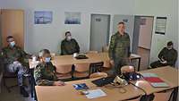 Soldaten im Feldanzug sitzen mit Abstand in einem Besprechungsraum. 