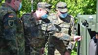 Drei Soldaten im Feldanzug inspizieren einen grünen Lastwagen.