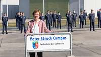 Brigitte Struck steht hinter dem Schild "Peter Struck Campus" in Faßberg.