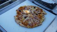 In Achtel geschnitte Pizza mit Kochschinken und schwarzen Oliven auf einem Ablagebrett