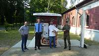 Männliche Person in Kochkleidung übergibt Pizza in geöffnetem Karton an männliche Person in Uniform vor einem Automaten
