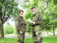 Feldwebel Jannis Siemer (li) und Hauptgefreiter Mats#de Staufenbiel (re) betrachten auf einer Wiese ein Dokument