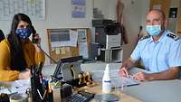 Ein Soldat und eine Zivilistin sitzen zusammen in einem Büro, auf dem Tisch vor ihnen liegen Akten.