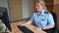 Eine Frau im Dienstanzug arbeitet in einem Büro an einem Computer.