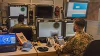 Ein deutscher und ein niederländischer Soldat sitzen vor Computern und mehreren Bildschirmen