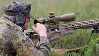 Ein Soldat liegt auf einer Wiese mit einem großen Gewehr im Anschlag.