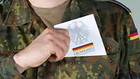 Soldat zieht Grundgesetzbuch aus der linken Brusttasche seiner Uniform.