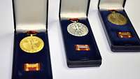 Drei Einsatzmedaillen der Bundeswehr in Gold, Silber und Bronze liegen in Schachteln nebeneinander.
