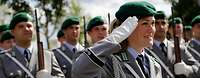 Soldatin des Wachbataillons legt ihre Hand zum Gruß an das Barett, im Hintergrund angetretene Soldaten