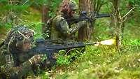 Zwei Soldaten liegen und knien auf dem Waldboden und schießen mit ihren Sturmgewehren.