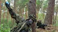 Ein Soldat wirft eine Handgranate. Ein anderer liegt mit einer Waffe im Anschlag sichert das Gelände