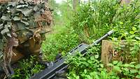 Auf dem Waldboden liegend beobachtet ein Soldat das dicht bewachsene Gelände vor ihm.