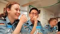 Eine Soldatin und zwei weitere Soldaten in blauer Arbeitsuniform sitzen an einem Tisch.