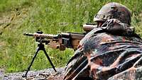 Ein Soldat liegt im Anschlag mit einem Gewehr, vor ihm ein Gurt mit Munition.