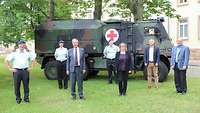 Mehrere Menschen mit und ohne Uniform vor einem militärischen Fahrzeug