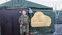 Oberstleutnant Matthias B. steht im Feldlager in Siauliai vor einem Schild mit dem Verbandswappen.