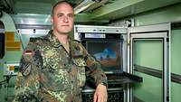 Soldat in Flecktarnuniform steht in einer lindgrünen Fernmeldekabine der Bundeswehr.