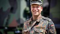 Ein Soldat in Flecktarnuniform steht vor einem Militär-Lkw und schaut in die Kamera.