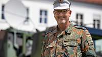 Ein Soldat mit Brille und Mütze der Gebirgsjägertruppe vor einem Militär-Lkw mit Antennenaufbauten