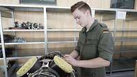 Ein junger Mann in einem olivgrünen Overall der Bundeswehr arbeitet an einem Gerät in einer Werkstatt