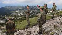 Fünf Soldaten stehen auf einer ebenen Fläche im Gebirge und schauen über die Berge.