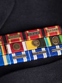 Ehrenzeichen als Bandschnallen an einer grauen Uniformjacke befestigt