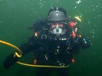 Interview Jessica Ritter Minentaucher Eine Person im Tauchanzug unter Wasser blickt direkt in die Kammera.