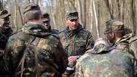 Sechs Soldaten stehen in einem Kreis im Wald. 
