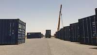 Zwischen Containern steht ein Sattelzug und ein Kran