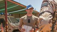 Ein Soldat mit blauem UN-Cap im Gespräch mit einem Kameraden, im Hintergrund Fahrzeuge der Bundeswehr 