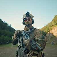 Ein Soldat mit Helm, Schutzbrille, Mund- und Gehörschutz hält eine Schrotflinte vor seiner Brust.