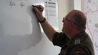 Stabsfeldwebel Penning steht vor einem Whiteboard und beschriftet es.