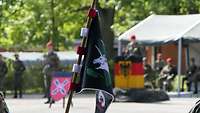 Auf einem schwarzen Wimpel ist ein silbernes Einhorn abgebildet. Im Hintergrund stehen mehrere Bundeswehrsoldaten.