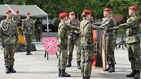 Sechs Soldaten halten ihre ausgestreckte Hand über eine schwarz-rot-goldene Truppenfahne.