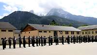 Die Rekruten in Uniformen stehen mit ausgebreiteten Armen auf dem Exerzierplatz nebeneinander.