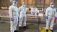 Ein Testteam in Vollschutz steht an der Abstrichstation und wartet auf die nächste Testperson im Auto.