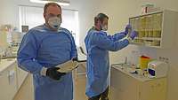 Zwei Männer in Schutzkleidung mit Schutzmaske bereiten Probenröhrchen vor