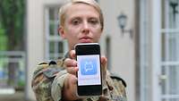 Eine Soldatin hält ein Smartphone mit dem eingeblendeten Messenger stashcat in die Kamera.