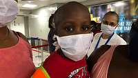 Das Adoptivkind ist mit Mundschutz am Flughafen zu sehen