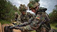 Zwei Soldaten setzen ein Gewehr aus Einzelteilen, die in einer Holzkiste liegen, zusammen. 