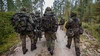 Vier Soldaten mit Gepäck marschieren und tragen einen verwundeten Soldaten bei einer Übung auf einem Waldweg. 