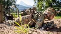 Zwei Soldaten gleiten mit ihrer Waffe unter Drähten entlang, die bodennah gespannt sind.