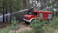 Ein Feuerwehr-Mann der Bundeswehr steht im Führerhaus eines Feuerwehr-Lastkraftwagen und löscht einen Waldbrand.