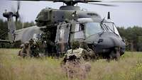 Ein Soldat kniet vor einem Hubschrauber und gibt dem Piloten Handzeichen.