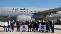 Personen vor dem Flugzeug halten Wappen der einzelnen gemeinnützigen Verbände hoch