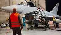 In einer Halle wird ein Eurofighter betankt. Ein Soldat überwacht den Betankungsvorgang.