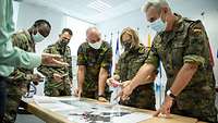 Five People from three different nations are standing on a desk with a map from Europe